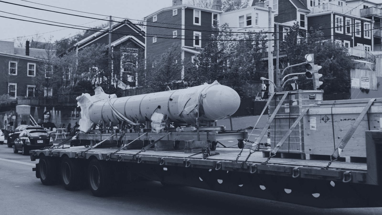 An oversize pressure vessel secured on a multi-axle flatbed moving through a residential street